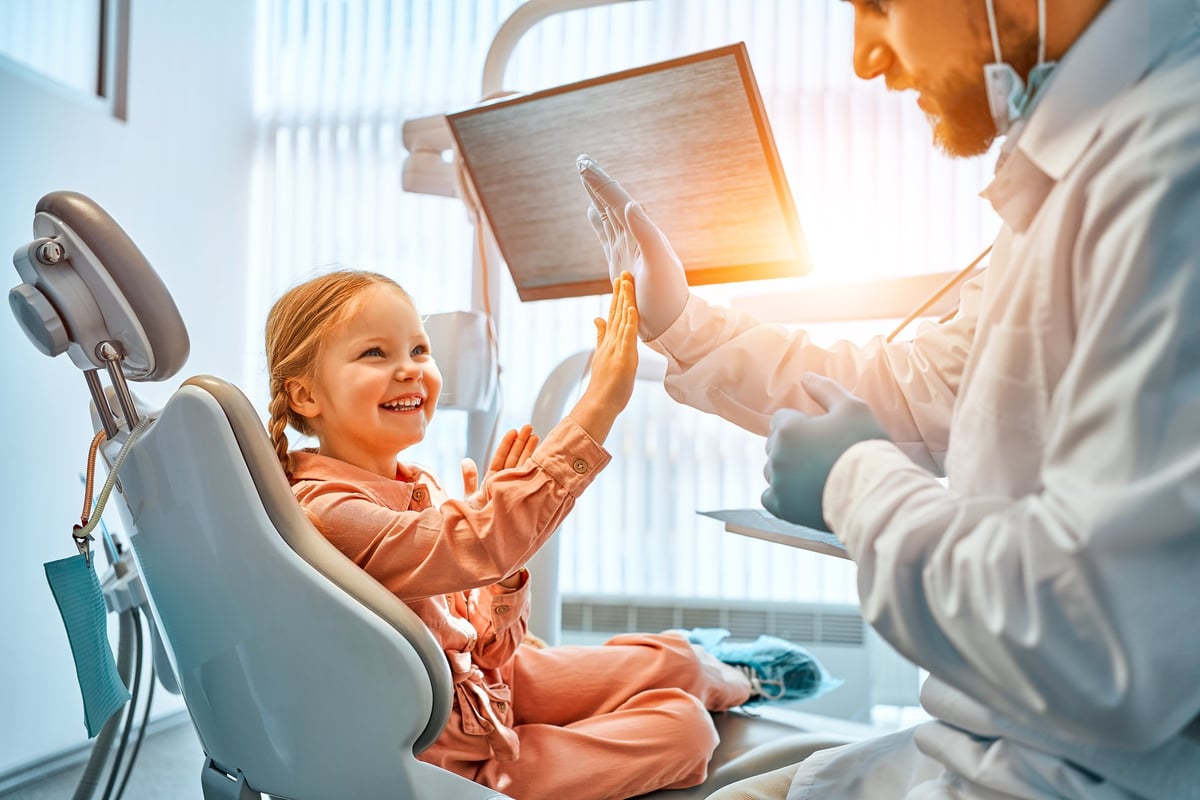 A little girl is sitting in a dentist's chair, giving a high five to the doctor and laughing. Children's dentistry.Sunlight.