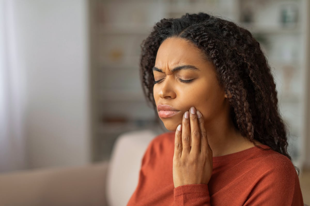 A young woman pressing her cheek, showing discomfort from a possible toothache at home