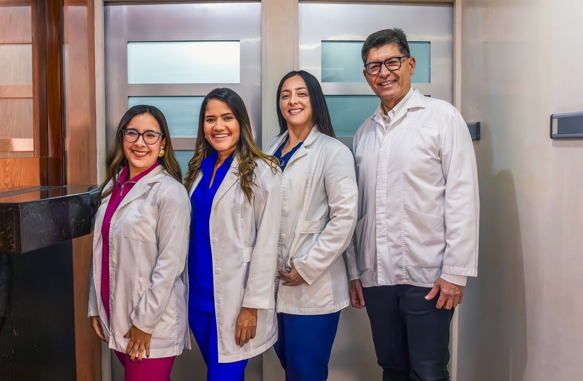 Group of four medical professionals standing in a clinic, smiling at the camera, wearing scrubs and lab coats