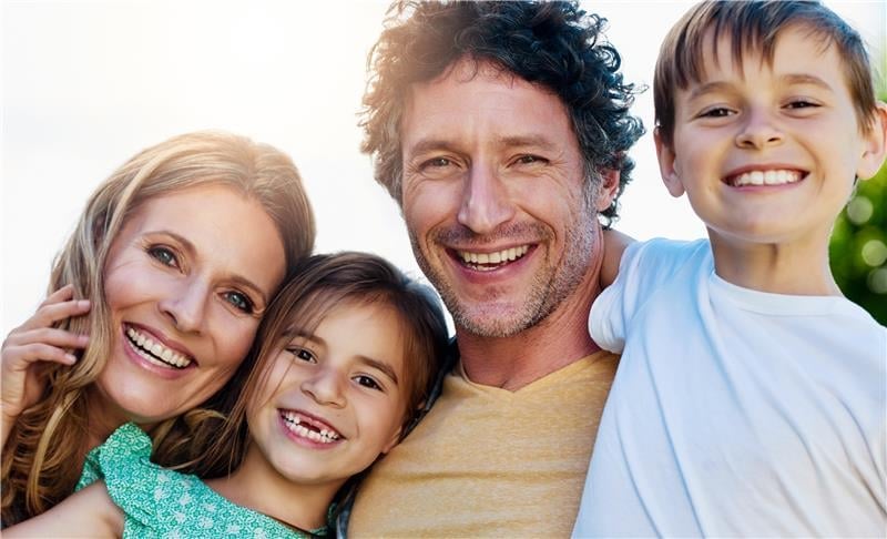 Happy family of four smiling together outdoors - two parents and two children