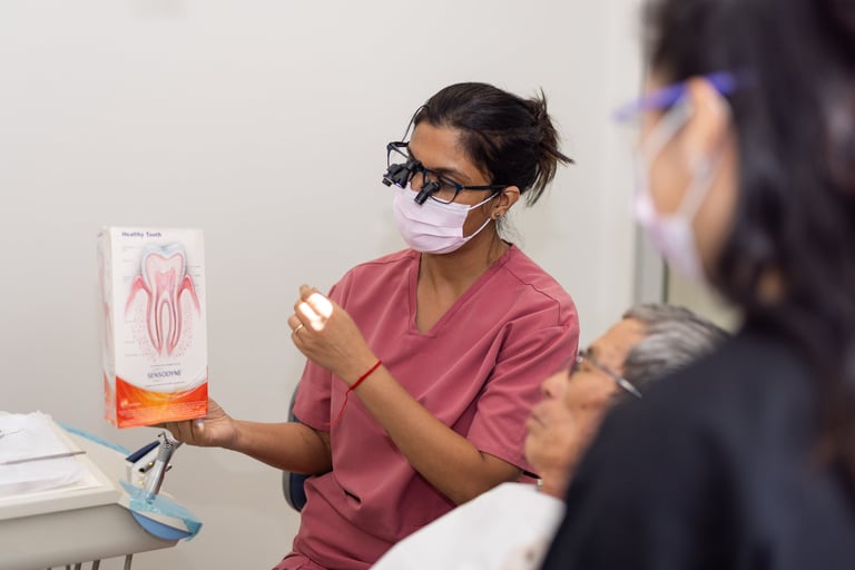 Female healthcare provider in burgundy scrubs and mask showing a dental anatomy model to a patient during a medical consultation.