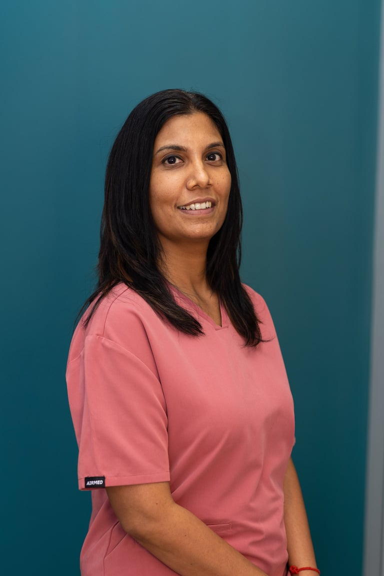 Woman with long black hair wearing a pink t-shirt smiling at the camera against a teal blue background