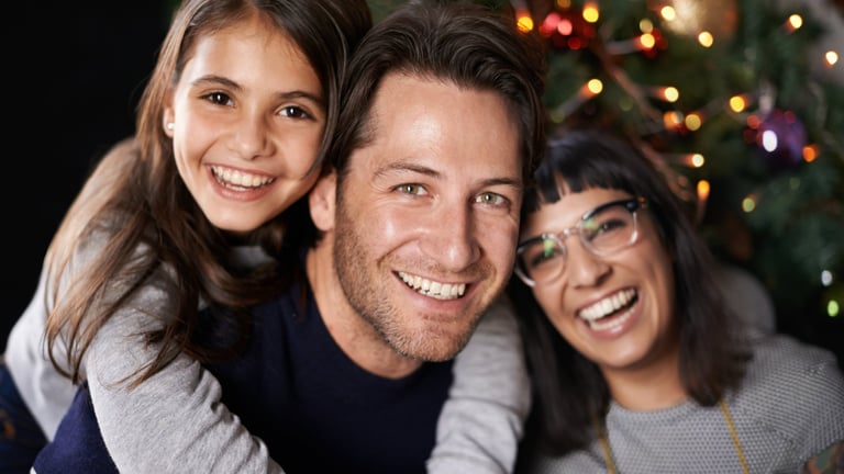 Man with two smiling women posing together in front of a decorated Christmas tree with twinkling lights